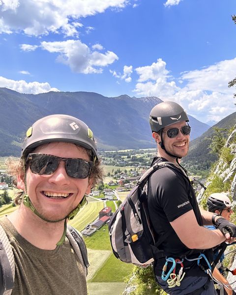 Two of the team on a via ferrata, mountains behind them